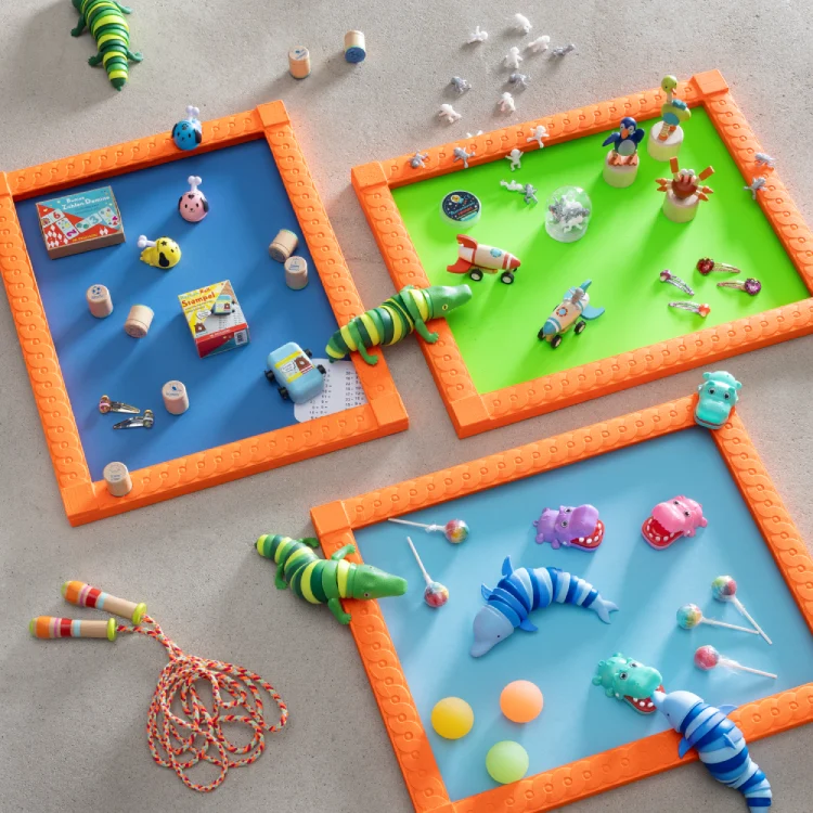 Viele bunte Spielsachen wie Flummis, Stempel, Stanzer, Wackeltiere, Lollies und ein Springseil sind auf dem Boden und auf grünen und blauen Farbflächen verteilt.