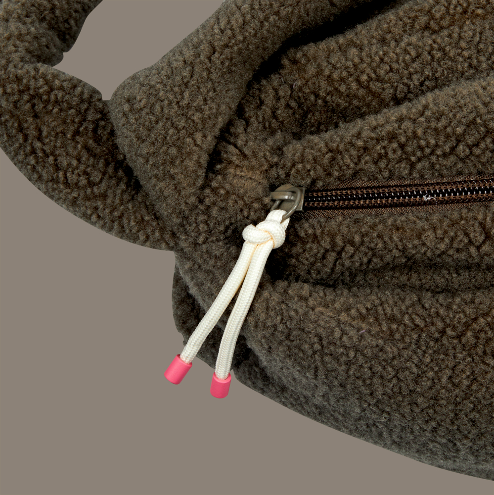 Nahaufnahme einer braunen Fleecetasche mit Reißverschluss und weißen Kordeln mit rosa Spitzen.