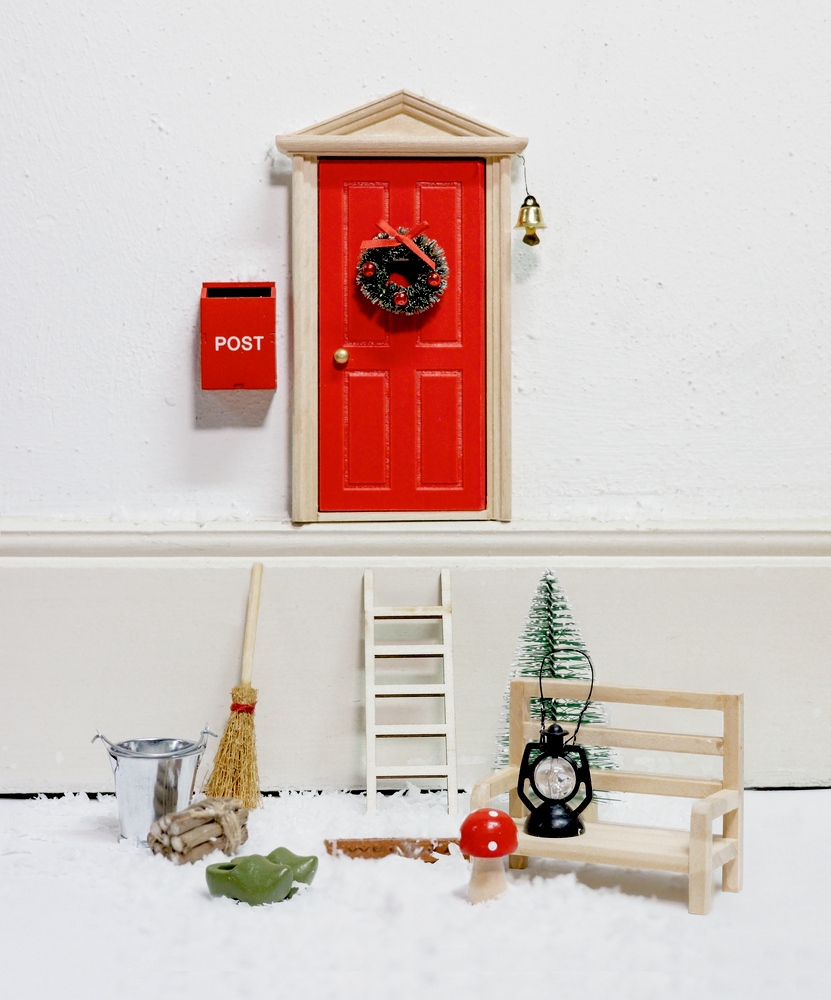 Rote Mini-Tür mit Türkranz, rotem Briefkasten, Leiter, Bank, Besen, kleinem Baum und Winterdekor auf weißem Hintergrund.