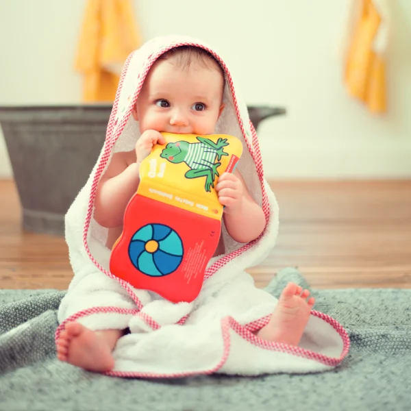 Baby in Badeponcho beißt in ein Badewannenbuch.