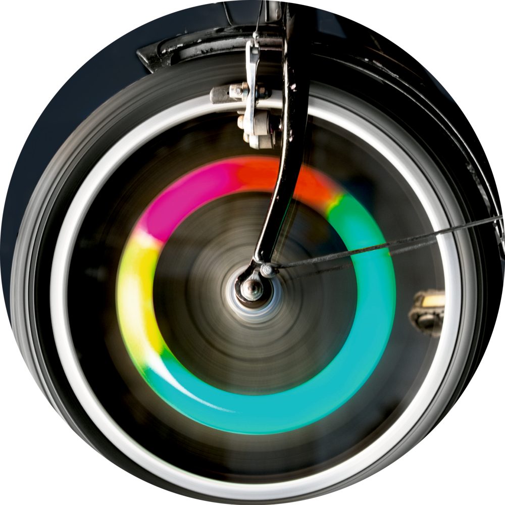 Nahaufnahme eines sich drehenden Fahrradrads mit einem leuchtenden Regenbogenmuster auf der Felge.