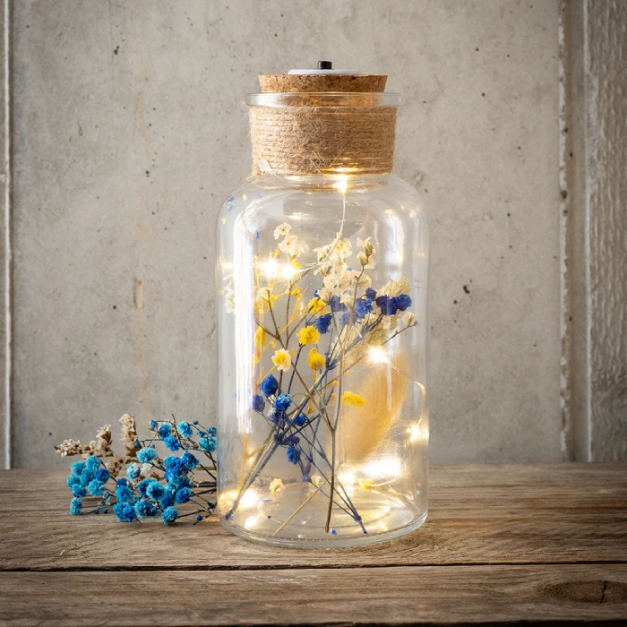 Glasflasche mit Korkdeckel darauf und einer Lichterkette und getrockneten Blumen darin