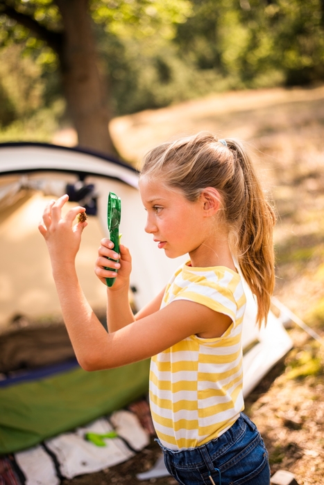 Nature Zoom Banner: Mädchen steht mit einer Lupe vor einem Zelt und beobachtet einen Gegenstand aus dem Wald